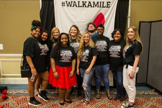 group of students standing posing with a walk a mile in her shoes backdrop